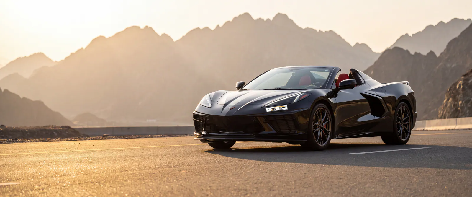 Black Chevrolet Corvette convertible from XGO Car Rental on the Hatta mountain road at sunset